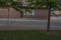 a lone parking meter near a brick building on the street with grass and trees in front