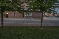 a lone parking meter near a brick building on the street with grass and trees in front