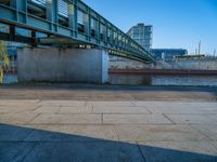 a skateboarder riding on a cement ramp next to a city street under a bridge