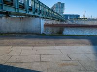 a skateboarder riding on a cement ramp next to a city street under a bridge