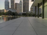 the walkway at the park leads to a lake and buildings in the background as evening falls