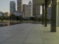 the walkway at the park leads to a lake and buildings in the background as evening falls