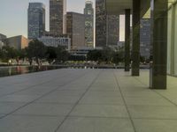 the walkway at the park leads to a lake and buildings in the background as evening falls