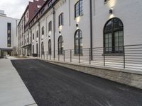 a paved street with buildings on both sides and a sidewalk beside it, next to a wall