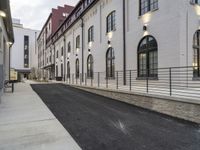 a paved street with buildings on both sides and a sidewalk beside it, next to a wall