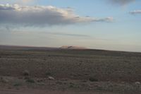 a dirt field next to the edge of an arid area, in the distance is a lone hill with a big sky