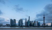 a man in a boat sits on the water, with the city buildings of shanghai towering in the background