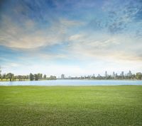 a nice view of a grassy field over water and the cityscape in the background