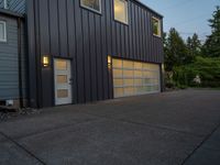 two gray garage doors and a paved driveway near trees and woods behind them a street light is on