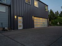 two gray garage doors and a paved driveway near trees and woods behind them a street light is on