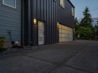 two gray garage doors and a paved driveway near trees and woods behind them a street light is on