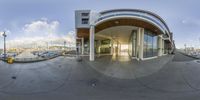 a 360 - lens fish eye shot of a boat dock by a glass building with lots of boats