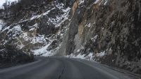 a road that is not paved and full of snow has steep rocks on either side