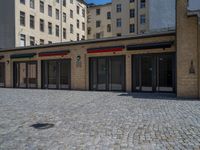 the sidewalk is paved with stones and has a bench in front of it, with no people inside