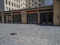 the sidewalk is paved with stones and has a bench in front of it, with no people inside