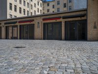 the sidewalk is paved with stones and has a bench in front of it, with no people inside