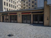 the sidewalk is paved with stones and has a bench in front of it, with no people inside