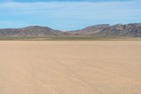 a boy in a hat is riding a motorcycle on a desert plain with mountains in the background