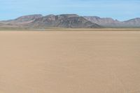 a boy in a hat is riding a motorcycle on a desert plain with mountains in the background