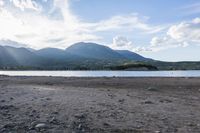 mountains in the distance near some water and rocks at low tide time in a body of water