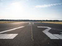 an empty runway with three people on a bike on it, with the sun beaming through the clouds