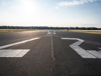 an empty runway with three people on a bike on it, with the sun beaming through the clouds