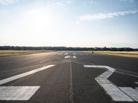 an empty runway with three people on a bike on it, with the sun beaming through the clouds