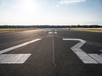 an empty runway with three people on a bike on it, with the sun beaming through the clouds