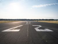 an empty runway with three people on a bike on it, with the sun beaming through the clouds