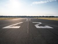 an empty runway with three people on a bike on it, with the sun beaming through the clouds