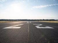 an empty runway with three people on a bike on it, with the sun beaming through the clouds