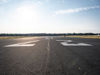 an empty runway with three people on a bike on it, with the sun beaming through the clouds