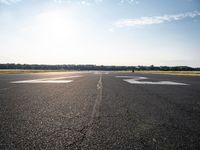 an empty runway with three people on a bike on it, with the sun beaming through the clouds