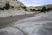 a dirt road that runs through the mountains near a stream of water and rocks on the edge