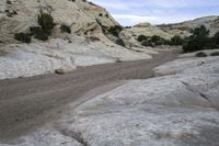 a dirt road that runs through the mountains near a stream of water and rocks on the edge