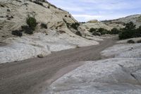 a dirt road that runs through the mountains near a stream of water and rocks on the edge