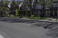 a paved sidewalk in front of a row of houses with trees and shrubs and bushes