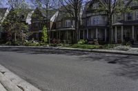 a paved sidewalk in front of a row of houses with trees and shrubs and bushes