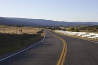 a white fence that surrounds the roadway and mountain range with a road to the front