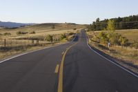 a white fence that surrounds the roadway and mountain range with a road to the front