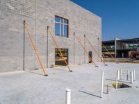 a very tall gray brick building sitting under construction while a fork and two pole in the foreground