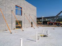 a very tall gray brick building sitting under construction while a fork and two pole in the foreground