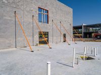 a very tall gray brick building sitting under construction while a fork and two pole in the foreground