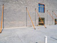 a very tall gray brick building sitting under construction while a fork and two pole in the foreground