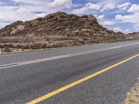 the empty street is on the rocky hill side and yellow paint shows the line of a curving road