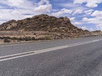 the empty street is on the rocky hill side and yellow paint shows the line of a curving road