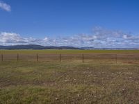 a large, empty field with some fence to protect it from falling grass in the distance is a long sky and large grassy field with clouds