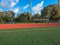 a man running on an outdoor track next to a flag pole and trees with blue skies