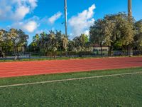 a man running on an outdoor track next to a flag pole and trees with blue skies