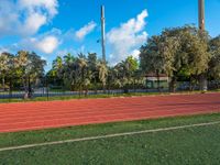 a man running on an outdoor track next to a flag pole and trees with blue skies